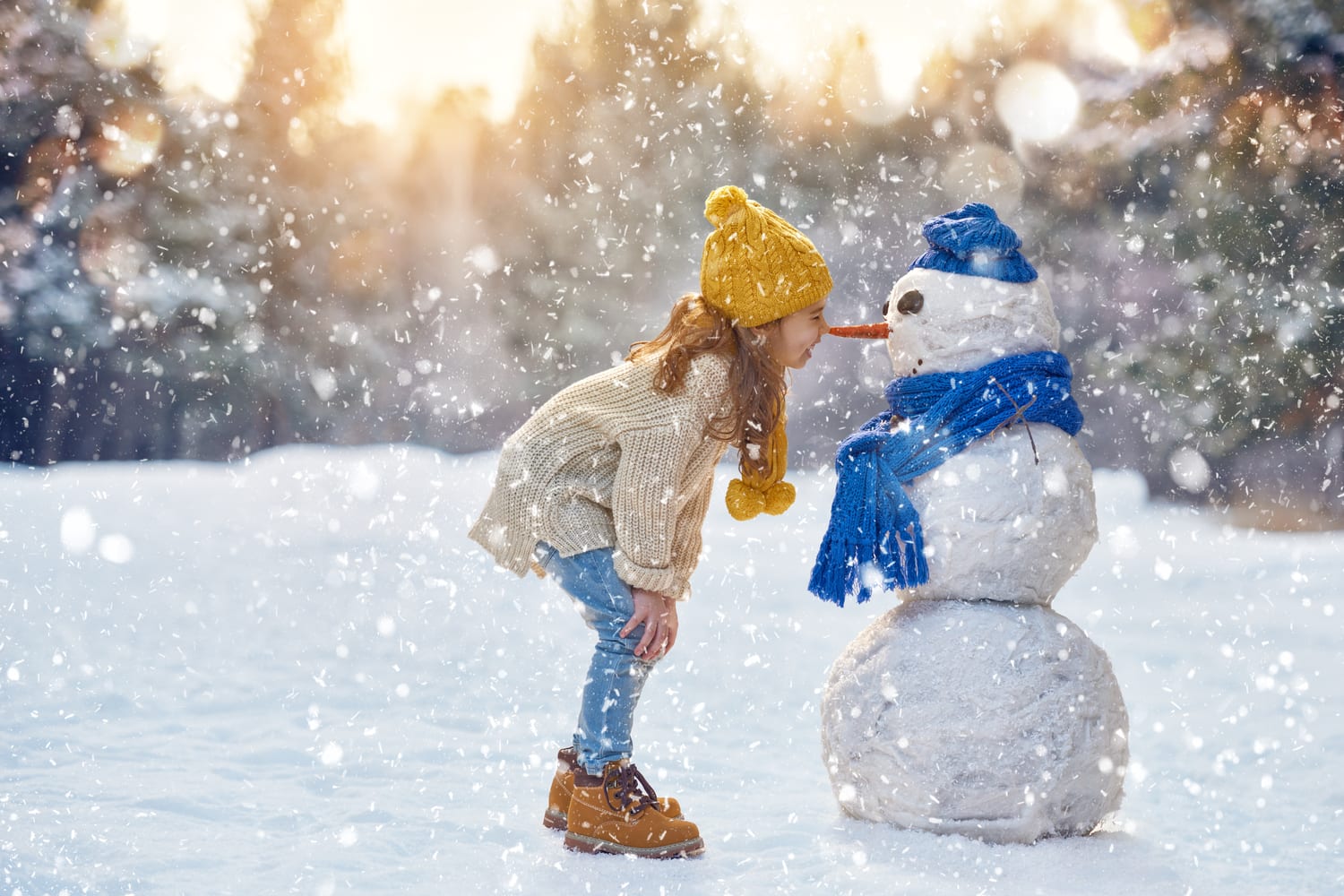 A young girl bends down to smile at a snowman in Winter Park, Colorado.
