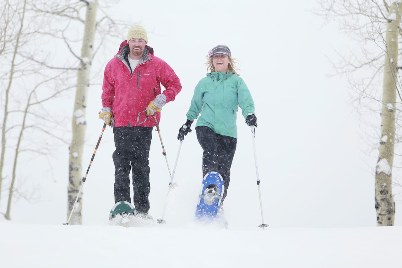 A joyous couple jubilantly strides while snowshoeing, one of the many Colorado winter activities in Grand County.